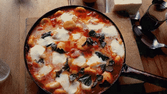 Gnocchi with mozzarella in tomato-basil sauce. It sits in a cast iron pan on a wooden chopping board. It looks staged.