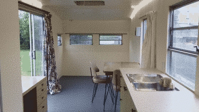 interior looking towards the front of the caravan. desk and kitchen are still visible, full table and otherwise empty.