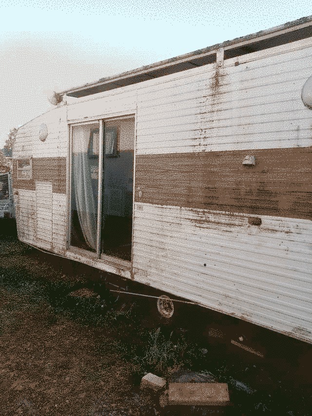 the front left exterior of the caravan pre renovation. Dirty white with a dusty brown strip across the middle.