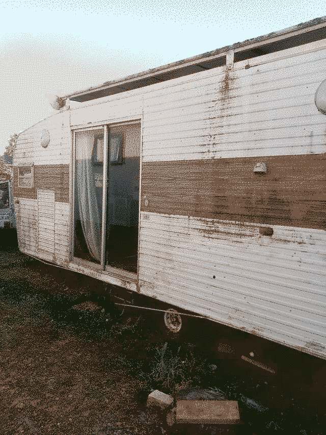 the left hand side of a 1976-ish Millard caravan. grimy, a small window and a double door, white corrugate with a brown band across the middle.