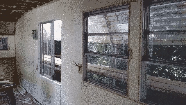 front right of the caravan with insulation on it. dappled sun and some scaffolding planks can be seen immediately through the window.